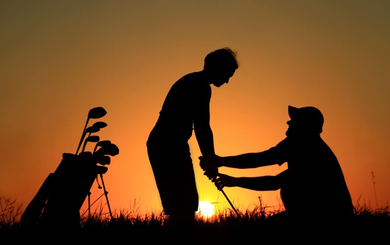 Golf Foot Placement - Your Foot Position for Golf Explained 9 one golfer helps another golfer with their swing against a sunset