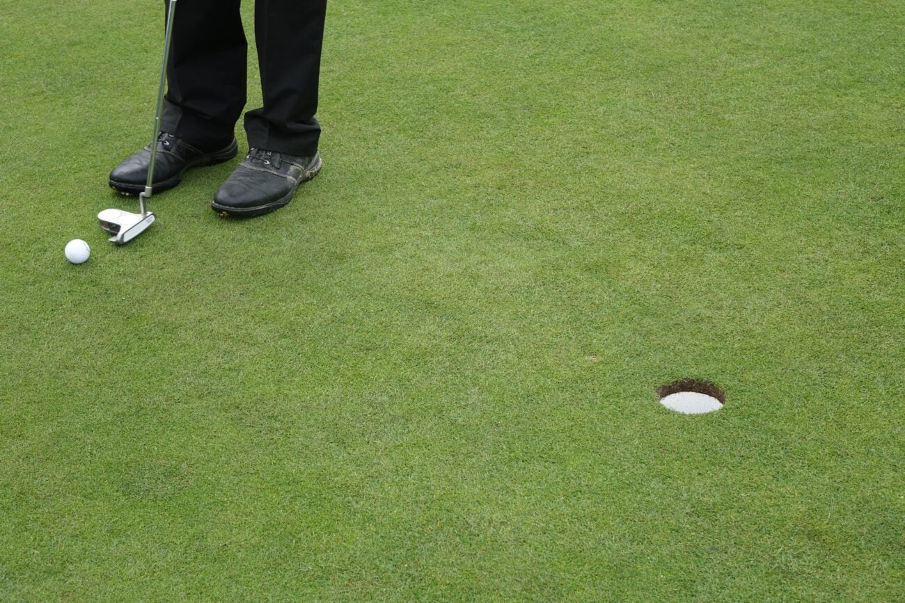 A golf putter resting on a putting green beside a ball, illustrating putter design and setup
